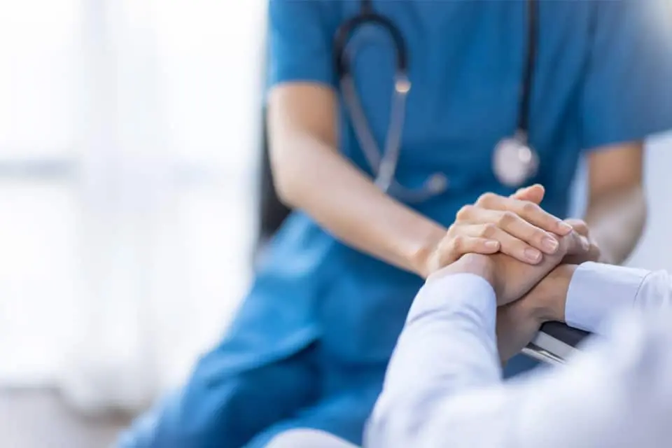 nurse in scrubs holding a patient's hands reassuringly